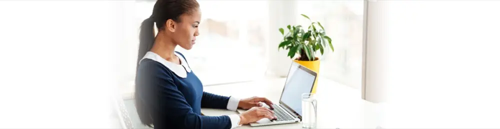 A woman working on a laptop beside a plant