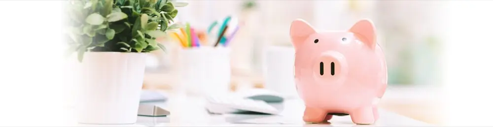 A piggy bank beside a plant and desk supplies